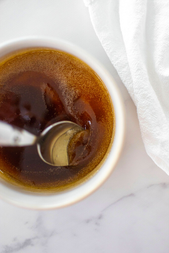 brown butter in a white bowl on a white marble counter with a spoon swirling it.
