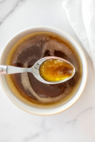 brown butter in a white bowl on a white marble counter with a spoon in it.