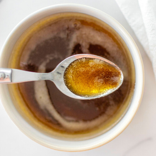 brown butter in a white bowl on a white marble counter with a spoon in it.