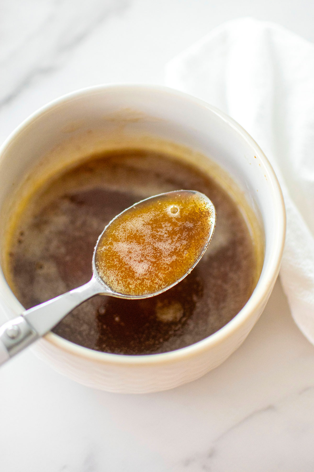 brown butter in a white bowl on a white marble counter with a spoon in it.
