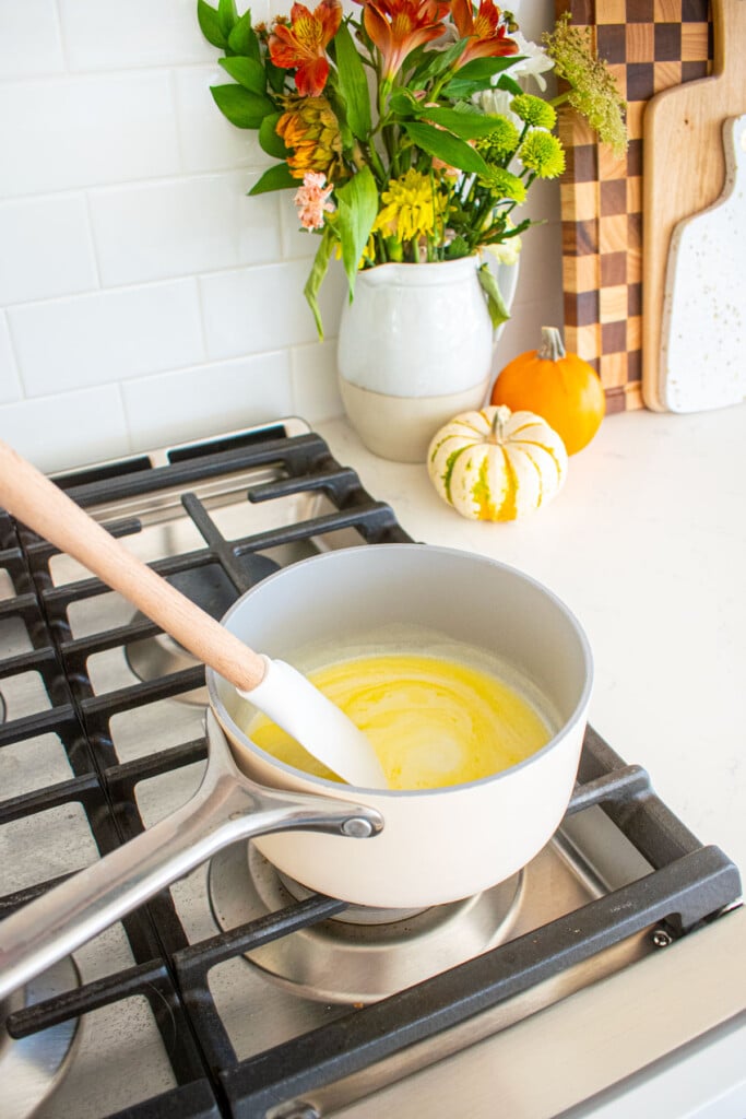 butter and milk being melted in a small pot over the stovetop being stirred with a spatula.