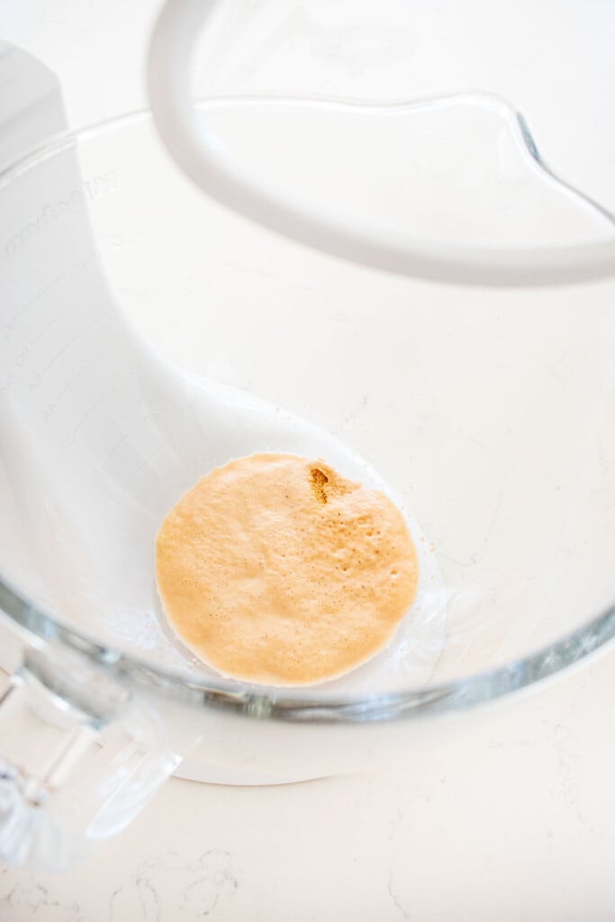 yeast bubbling in a glass mixing bowl on a mixer with the dough hook.