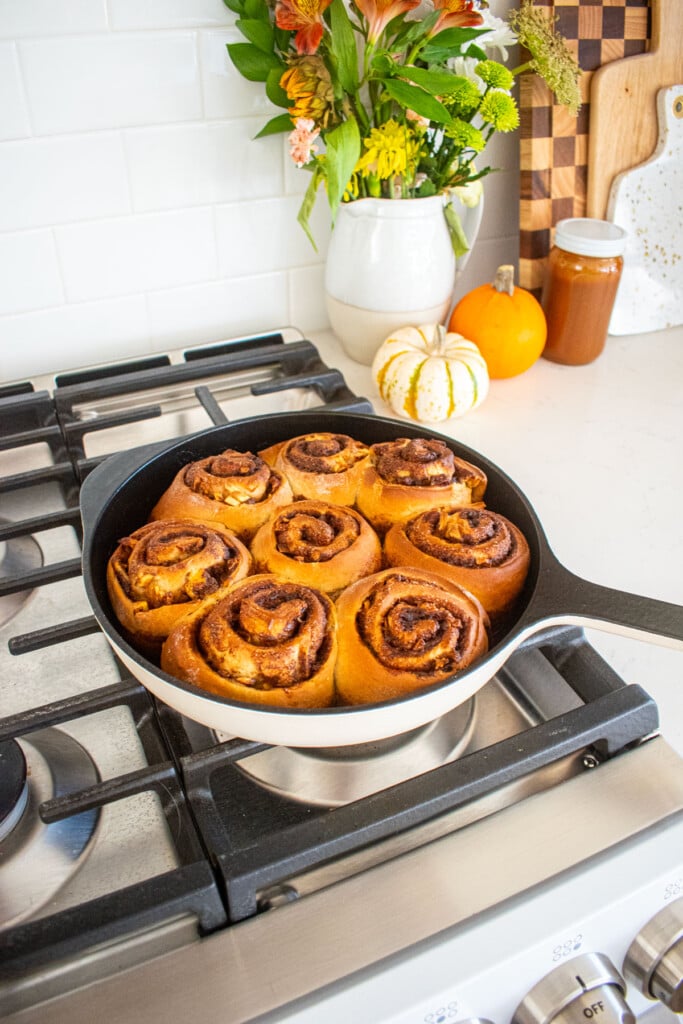 baked caramel apple pie cinnamon rolls in a cast iron skillet cooling on top of an oven.