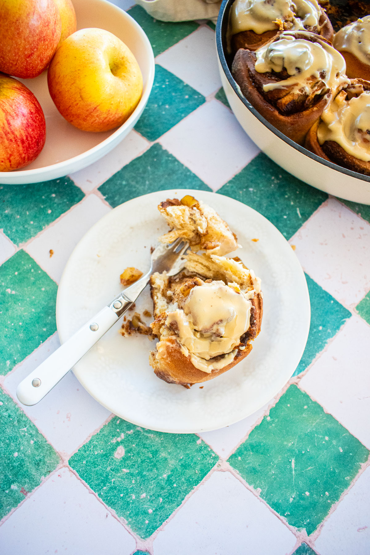 caramel apple pie cinnamon roll with a fork on a plate on a tile table.