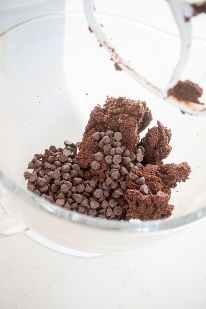double chocolate pumpkin cookie dough with chocolate chips in a glass mixing bowl on a white marble counter.