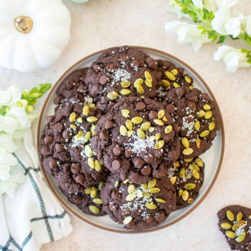 double chocolate pumpkin cookies on a plate with pumpkins and fresh flowers.