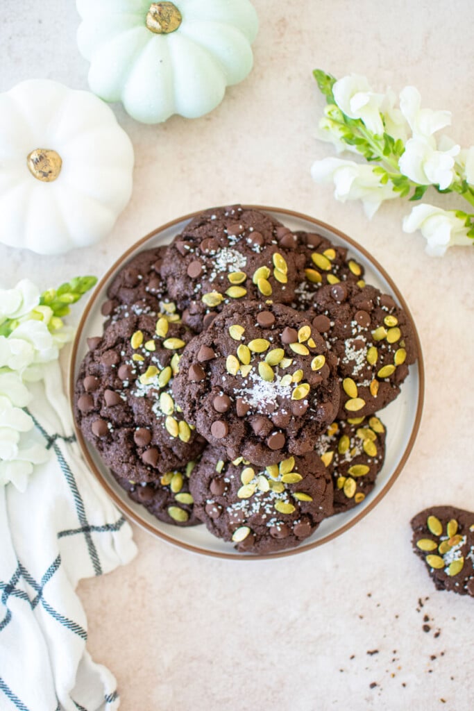 double chocolate pumpkin cookies on a plate with pumpkins and fresh flowers.