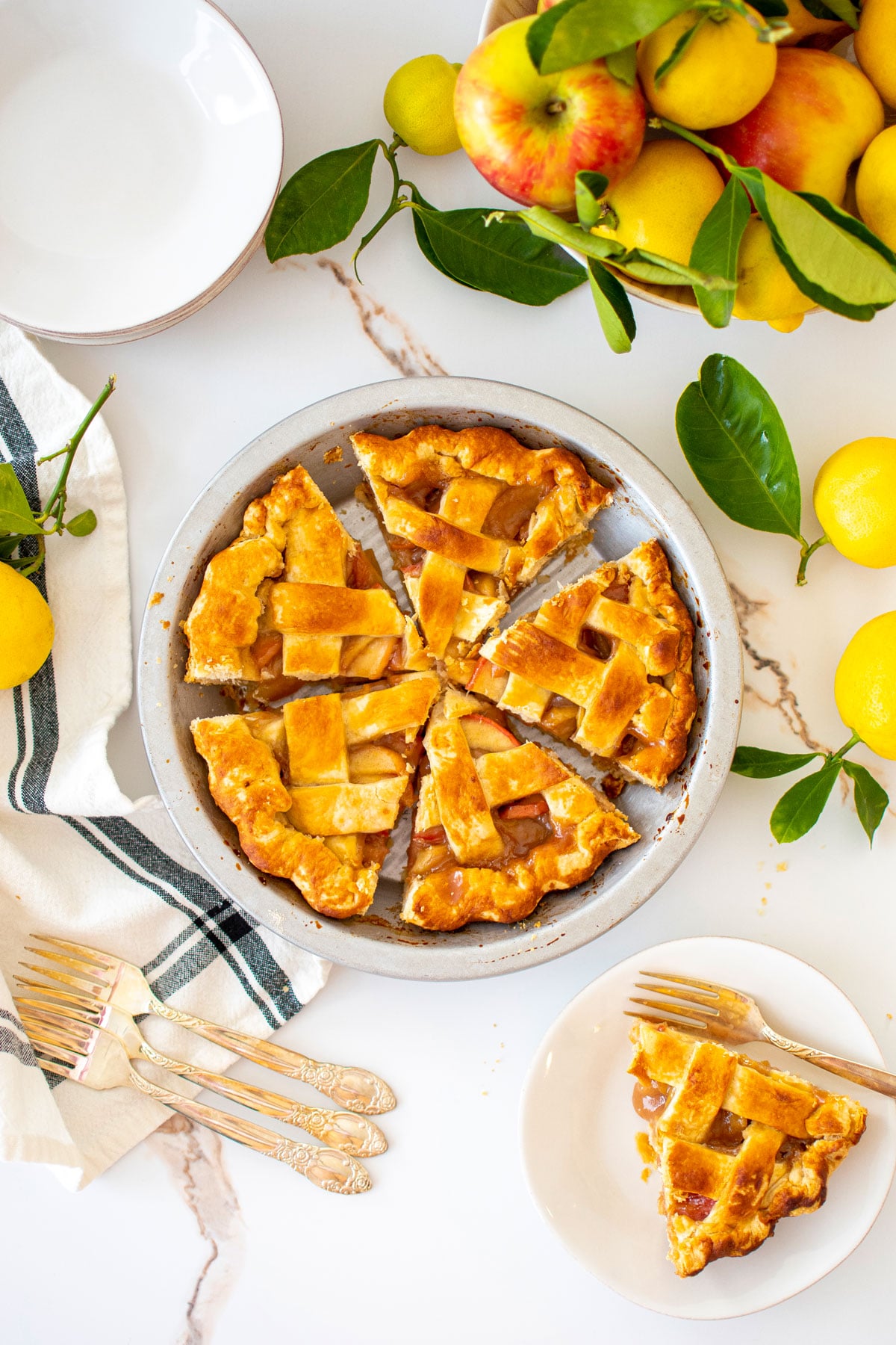 honey lemon apple pie in a aluminum pie pan on a white marble counter with apples and lemons.