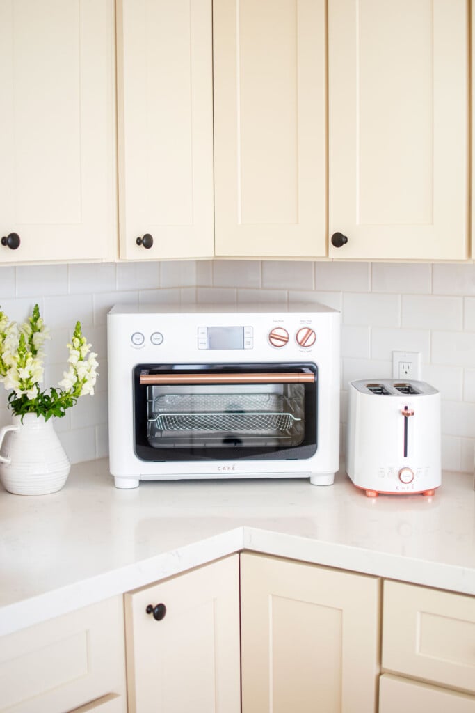 white countertop oven on a white marble kitchen counter with tan cabinets.