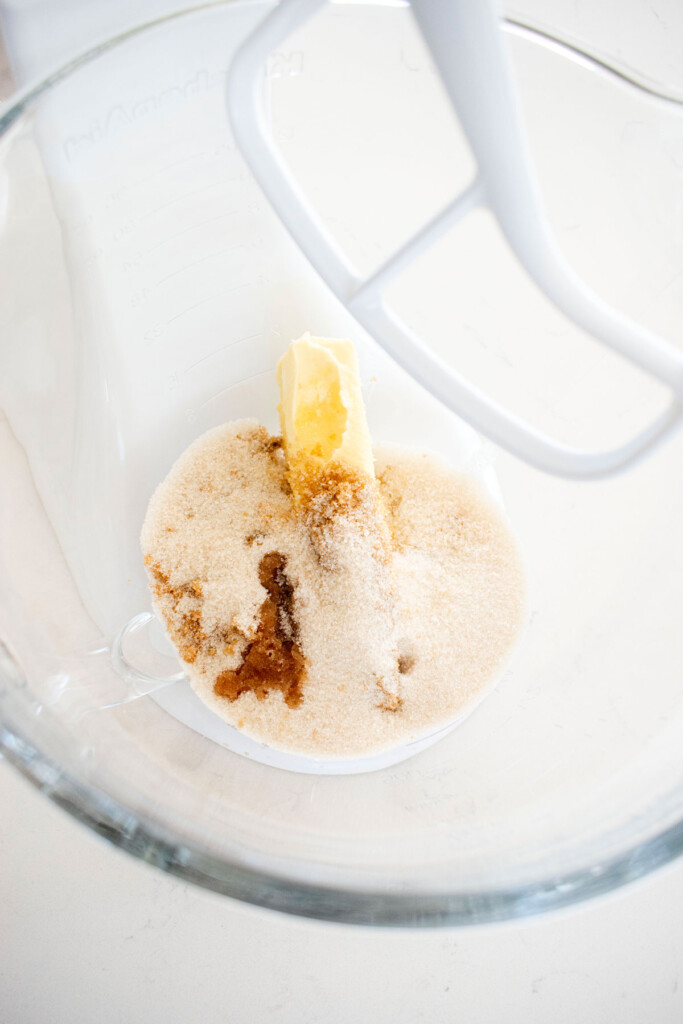 butter and sugar in a glass mixing bowl on a white marble counter.
