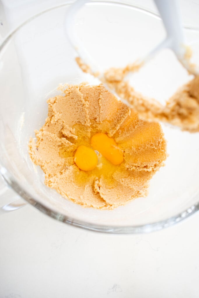 creamed butter and sugar with eggs in a glass mixing bowl on a white marble counter.