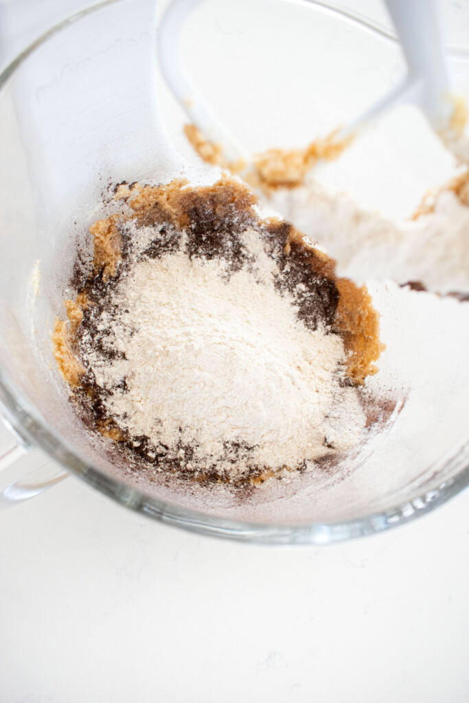 ingredients for organic halloween cookies in a glass mixing bowl on a white marble counter.