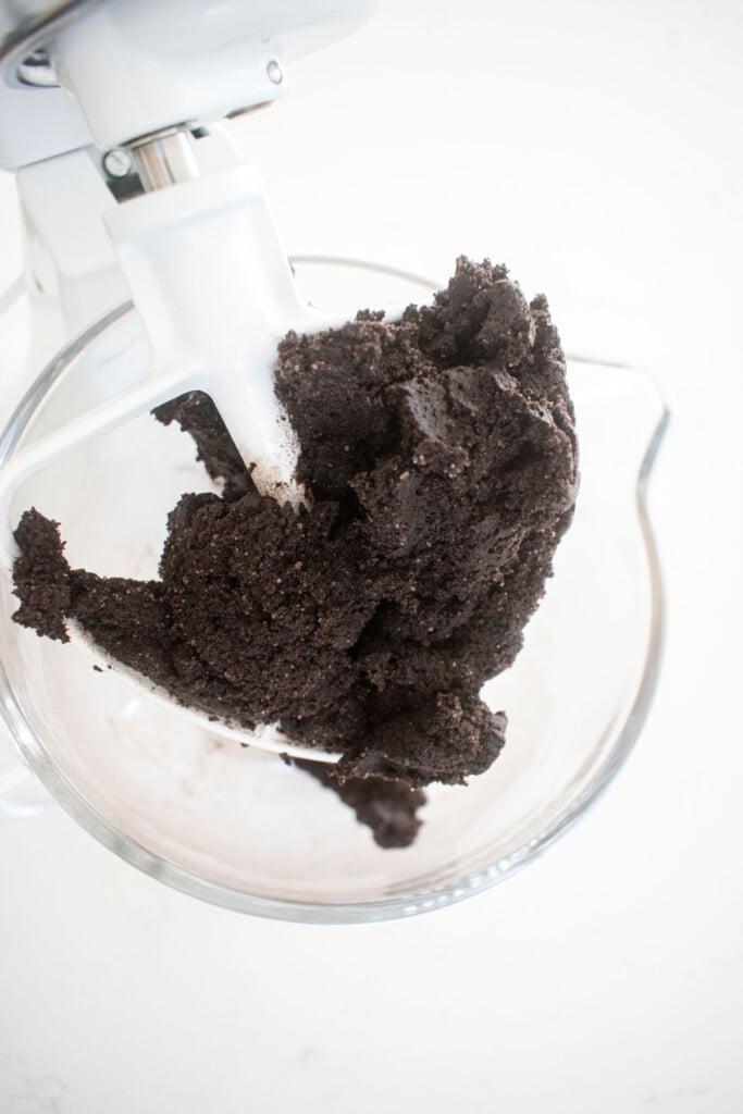 black cocoa cookie dough in a glass mixing bowl on a white marble counter.