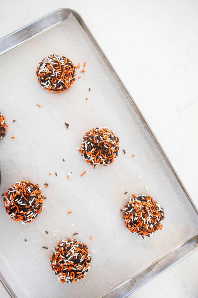 organic halloween cookie dough rolled in sprinkles on a baking sheet on a white marble counter.
