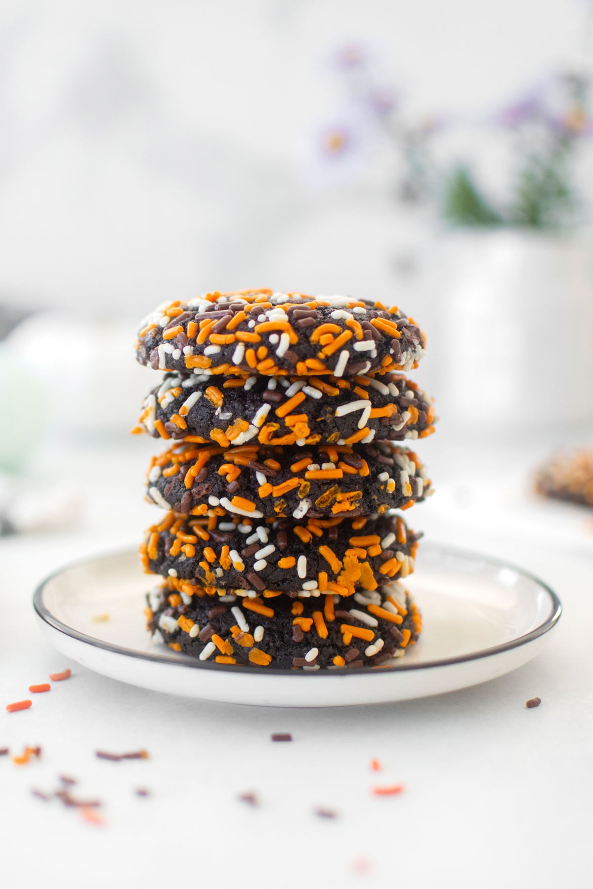 organic halloween cookies on a white plate on a white marble counter with flowers and pumpkins.