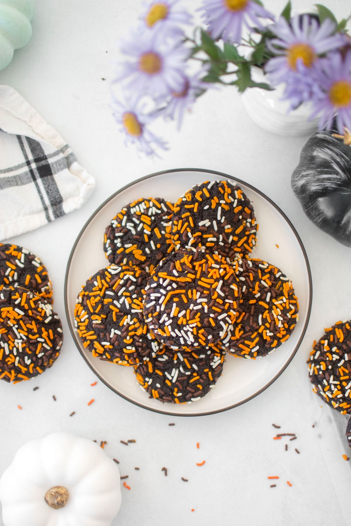 organic halloween cookies on a white plate on a white marble counter with flowers and pumpkins.