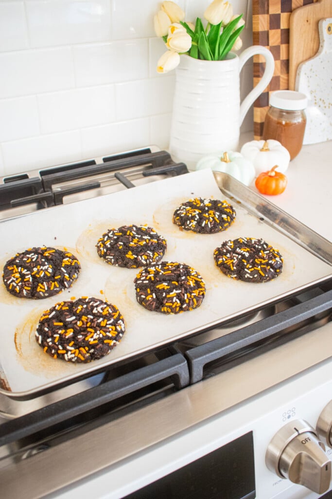 baking sheet cooling on top of oven with halloween cookies with sprinkles on it.