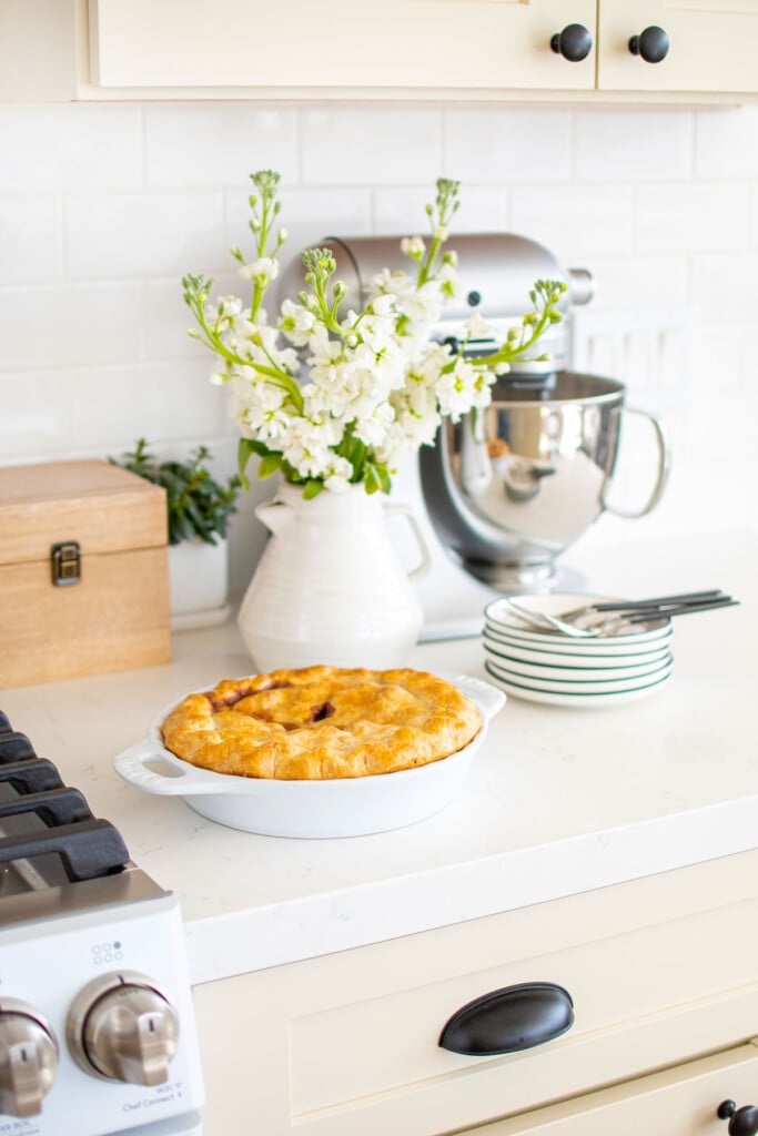 berry pie on a kitchen countertop with flowers and pie plates.
