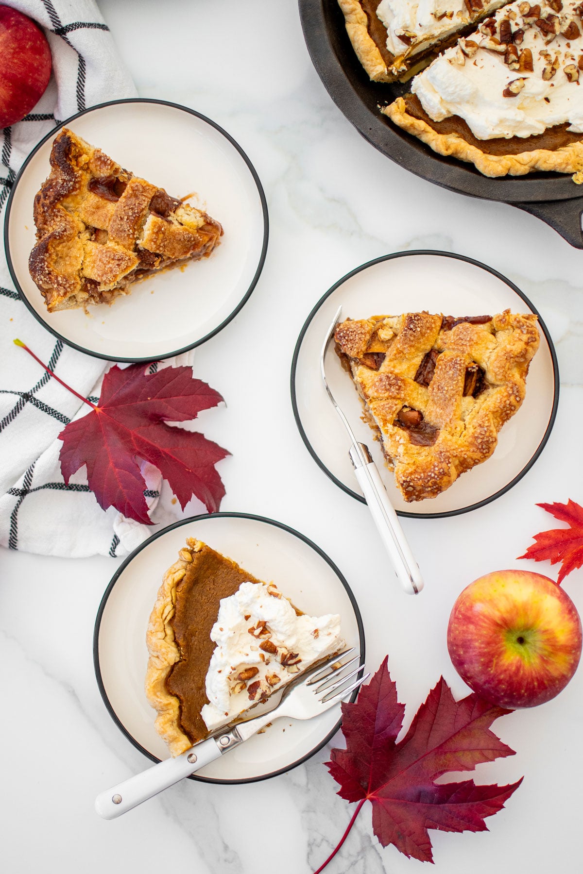 fall pie slices on a plates on a white marble counter with fall maple leaves.