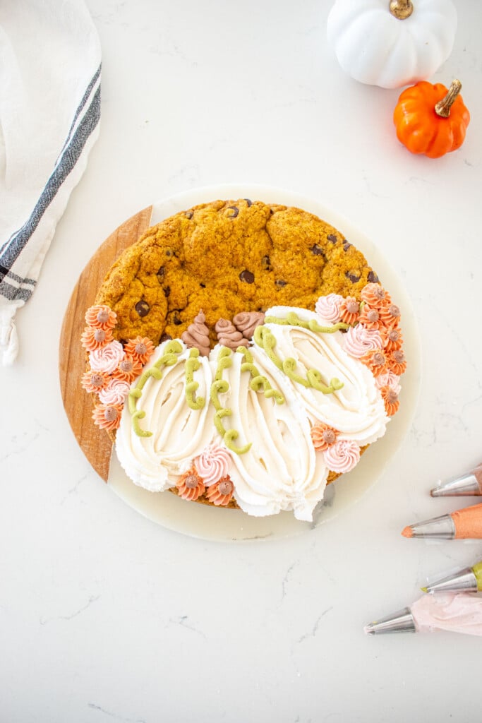 pumpkin chocolate chip cookie cake with decorated frosting pumpkins on a white marble counter.