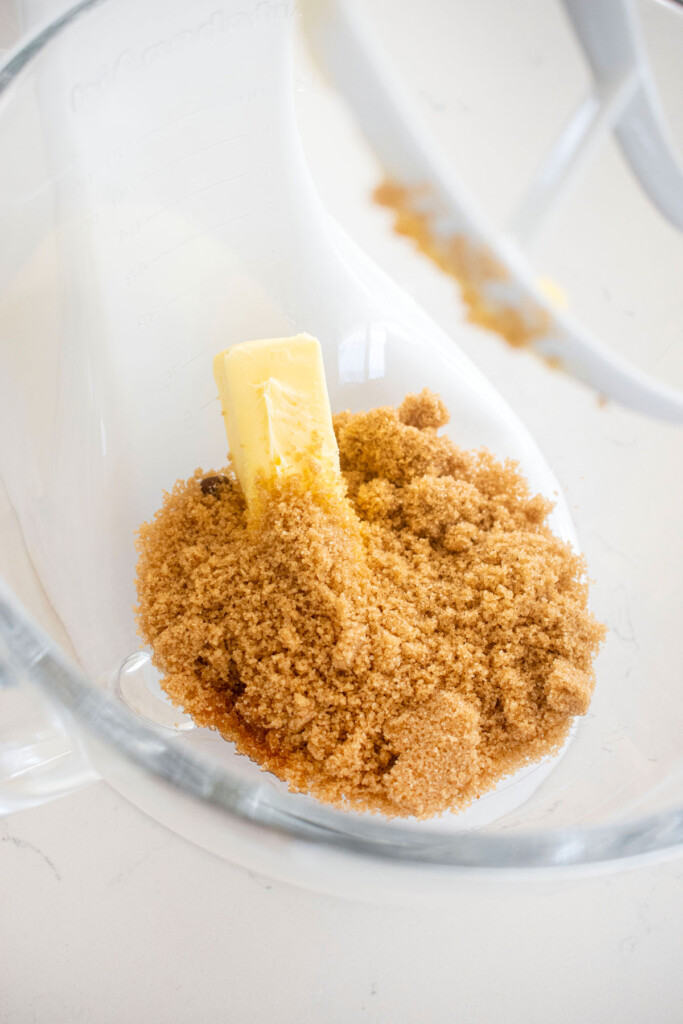 butter and brown sugar in a glass mixing bowl on a white marble counter.