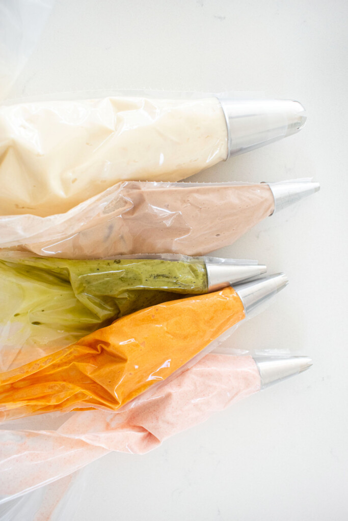 piping bags with colored frosting on a white marble counter.