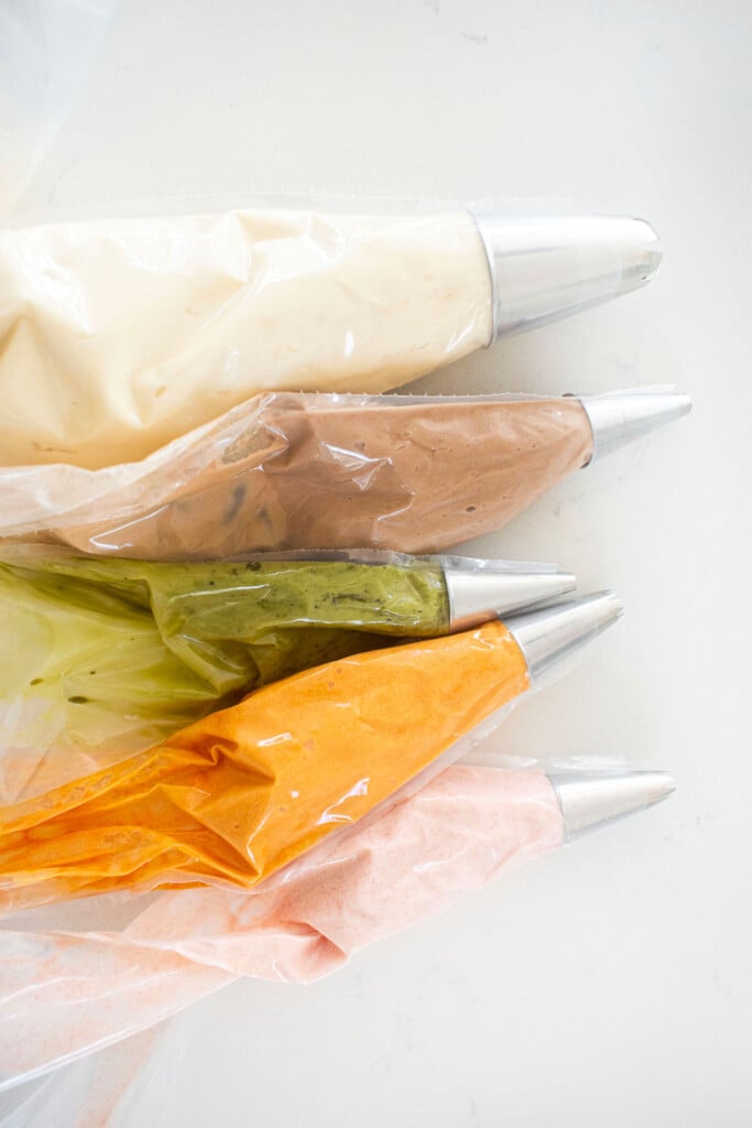 piping bags with colored frosting on a white marble counter.