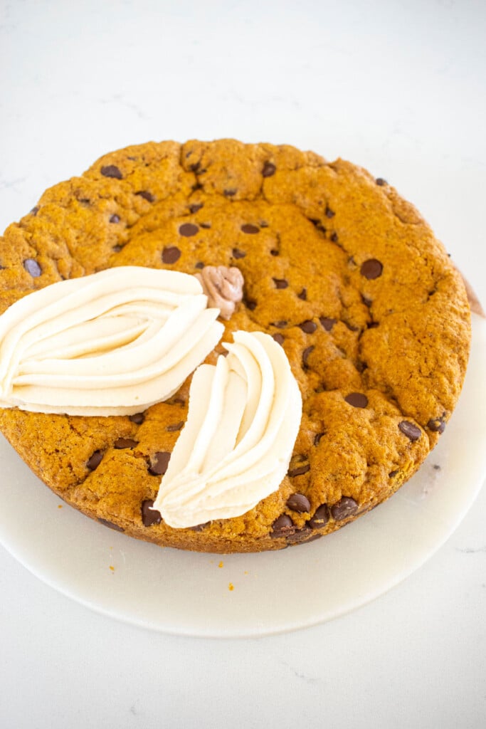 white frosting pumpkins being piped onto a pumpkin chocolate chip cookie cake on a marble counter.