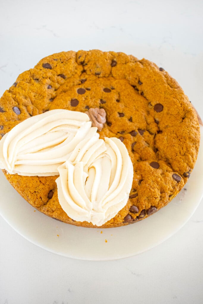 white frosting pumpkins being piped onto a pumpkin chocolate chip cookie cake on a marble counter.