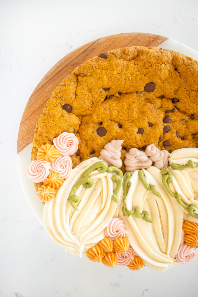 pumpkin chocolate chip cookie cake with decorated frosting pumpkins on a white marble counter.