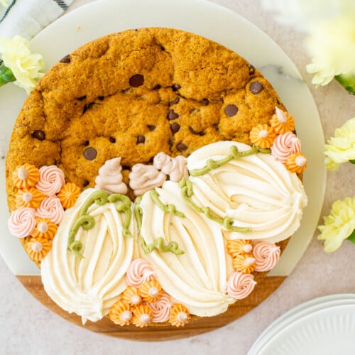 pumpkin chocolate chip cookie cake with piped buttercream pumpkins on a white marble serving board with fresh flowers.
