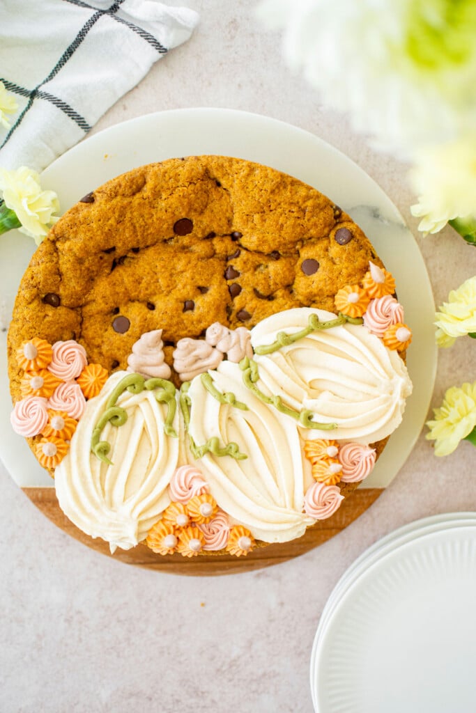 pumpkin chocolate chip cookie cake with piped buttercream pumpkins on a white marble serving board with fresh flowers.