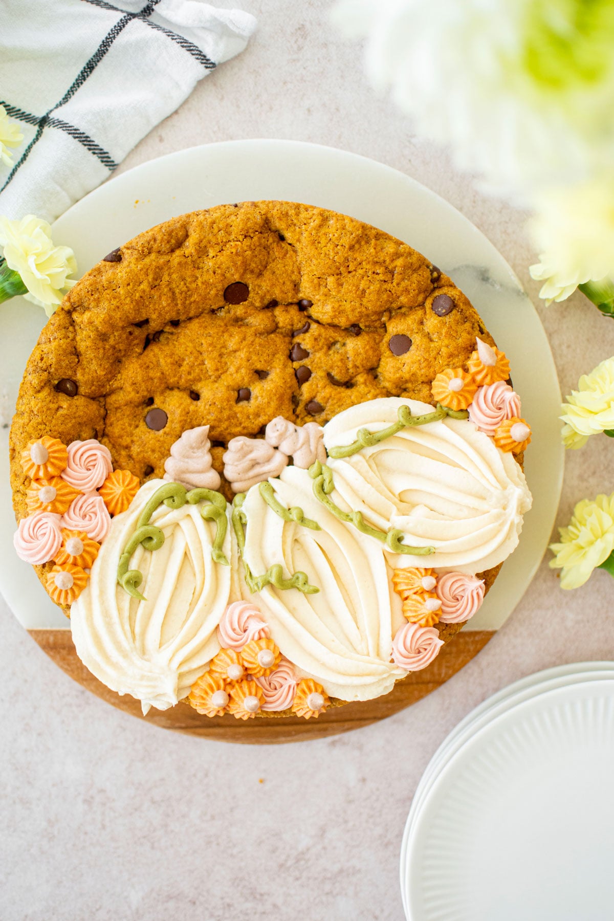 pumpkin chocolate chip cookie cake with piped buttercream pumpkins on a white marble serving board with fresh flowers.