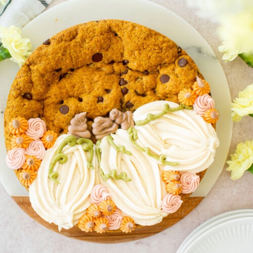 pumpkin chocolate chip cookie cake with buttercream pumpkins and small rosettes on a table with flowers.