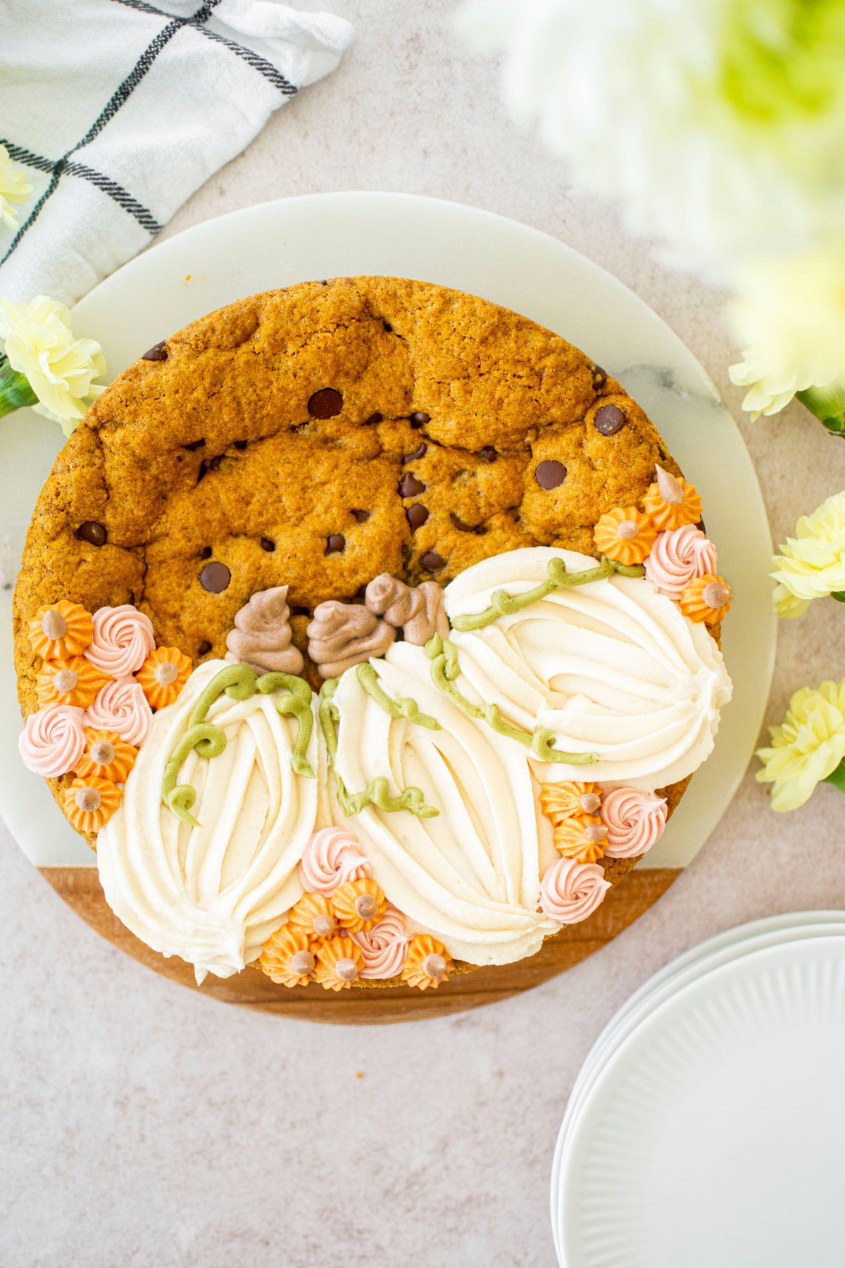 pumpkin chocolate chip cookie cake with buttercream pumpkins and small rosettes on a table with flowers.