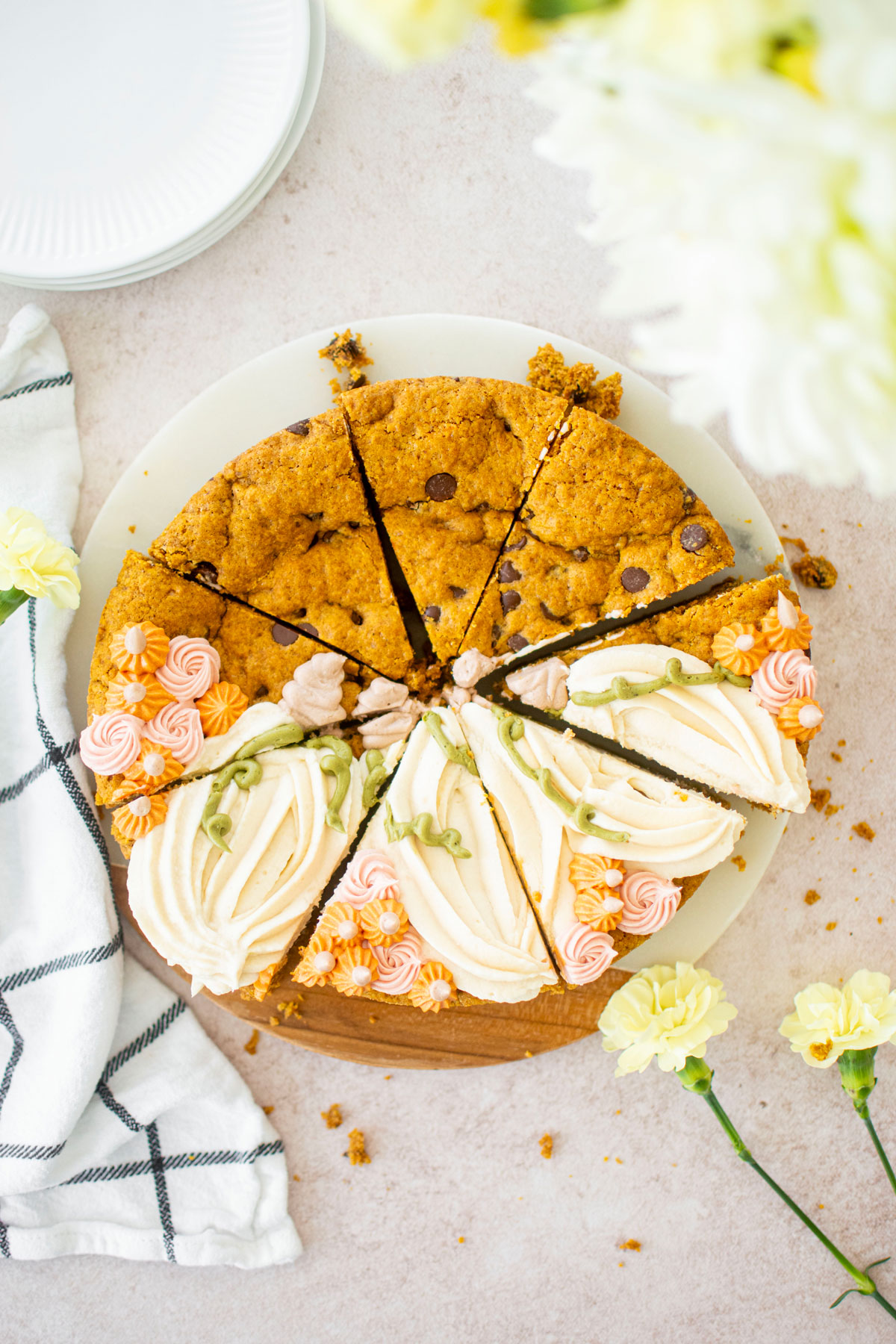 sliced pumpkin chocolate chip cookie cake with piped buttercream pumpkins on a white marble serving board with fresh flowers.