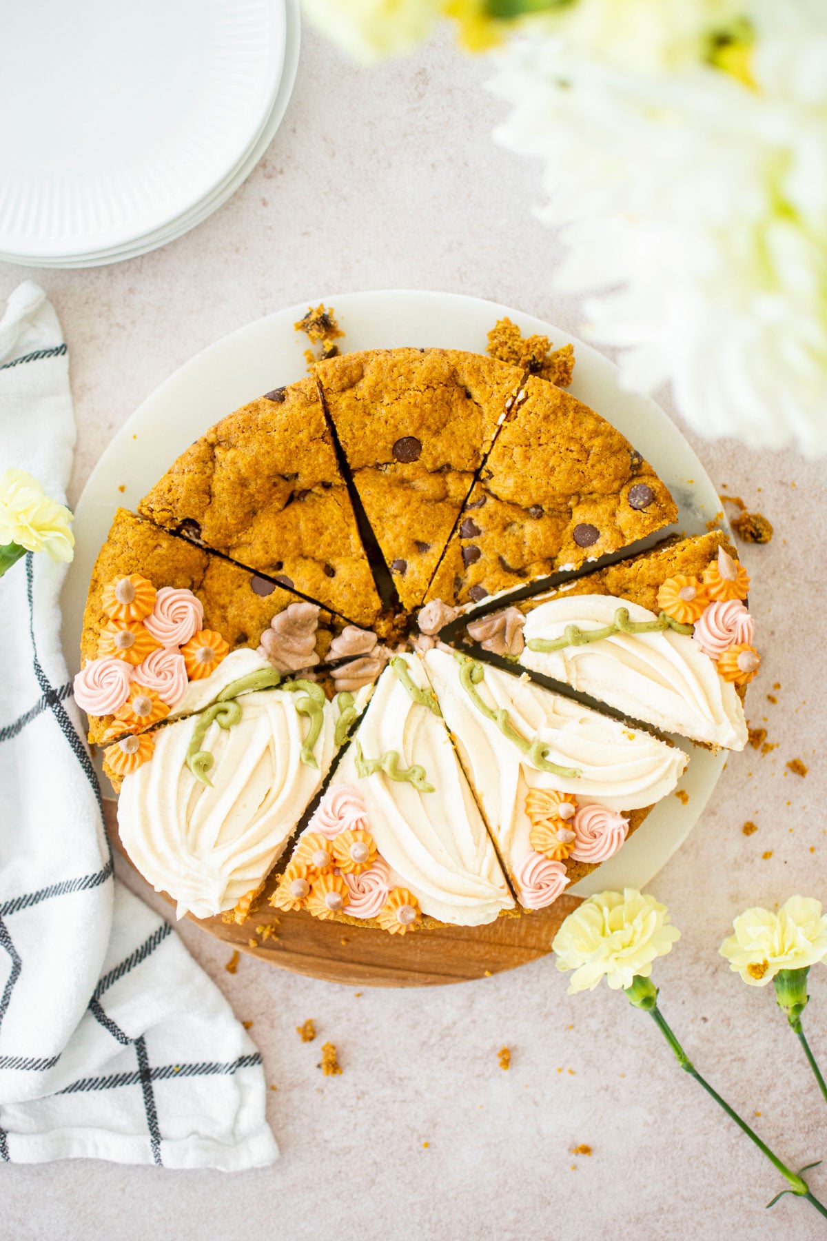pumpkin chocolate chip cookie cake with buttercream pumpkins and small rosettes on a table with flowers cut into slices.