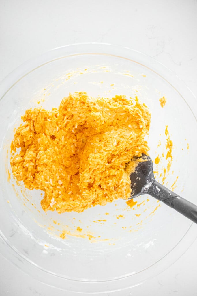 pumpkin donuts for dogs batter mixed together in a glass mixing bowl on a white marble countertop.