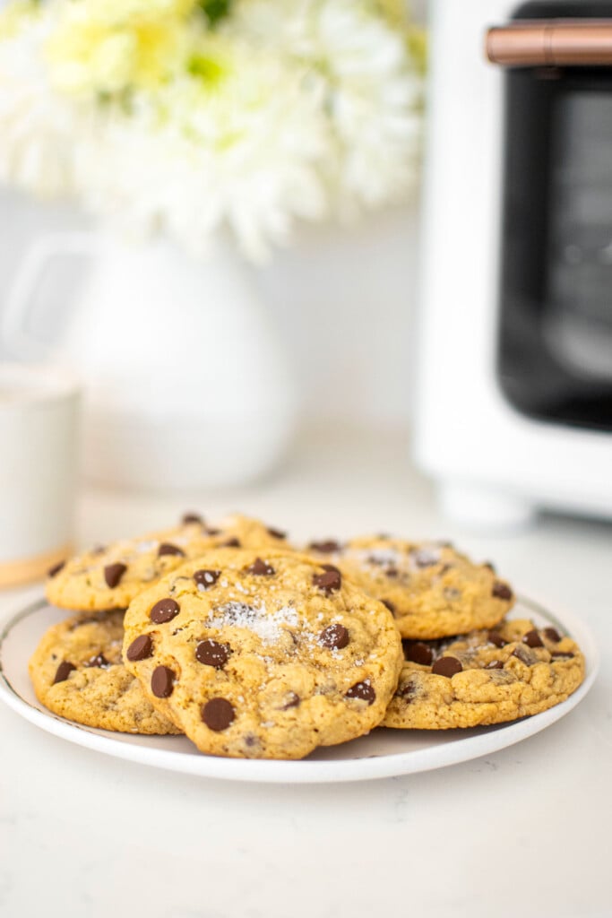 maple brown sugar cookies on a plate on a marble counter with white flowers and a mug.