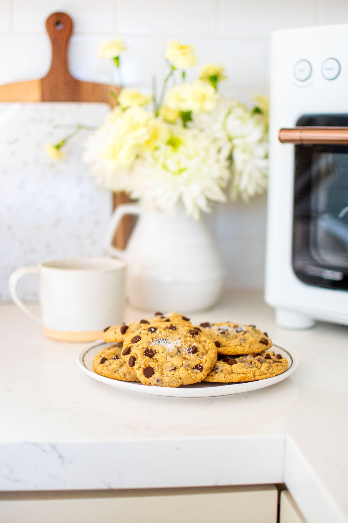 maple brown sugar cookies on a plate on a marble counter with white flowers and a mug.