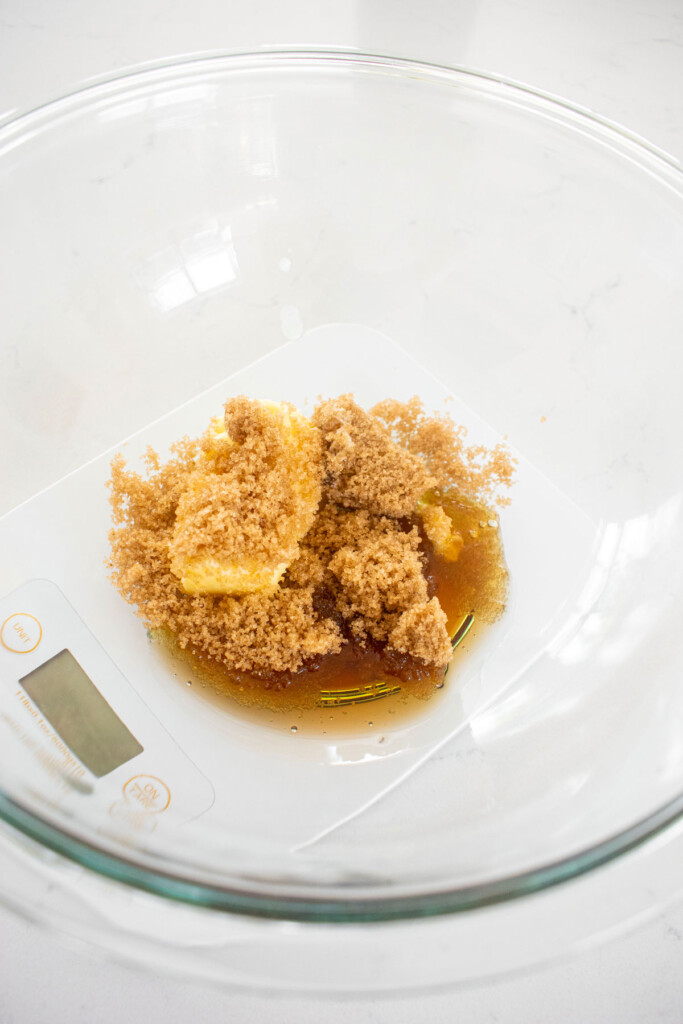 butter, brown sugar and maple syrup in a glass mixing bowl on a scale.