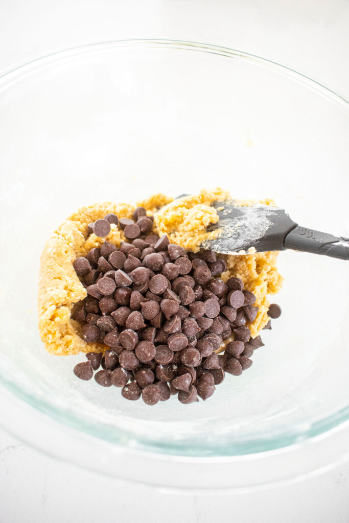 maple brown sugar cookie dough with chocolate chips in a glass bowl on a white marble counter.