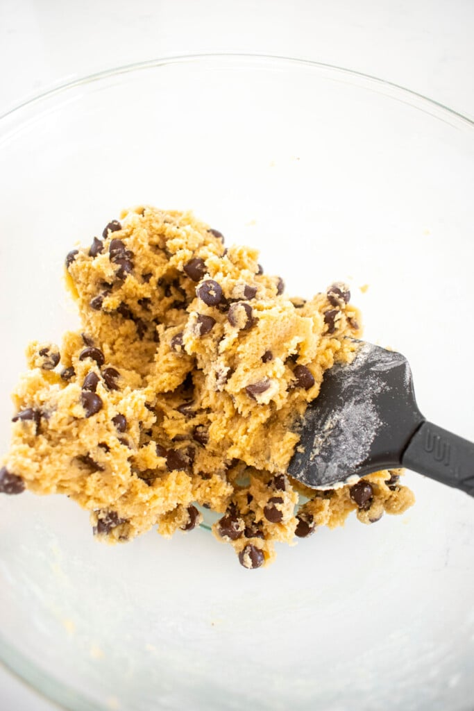 maple brown sugar cookie dough with chocolate chips in a glass mixing bowl on a white marble counter.