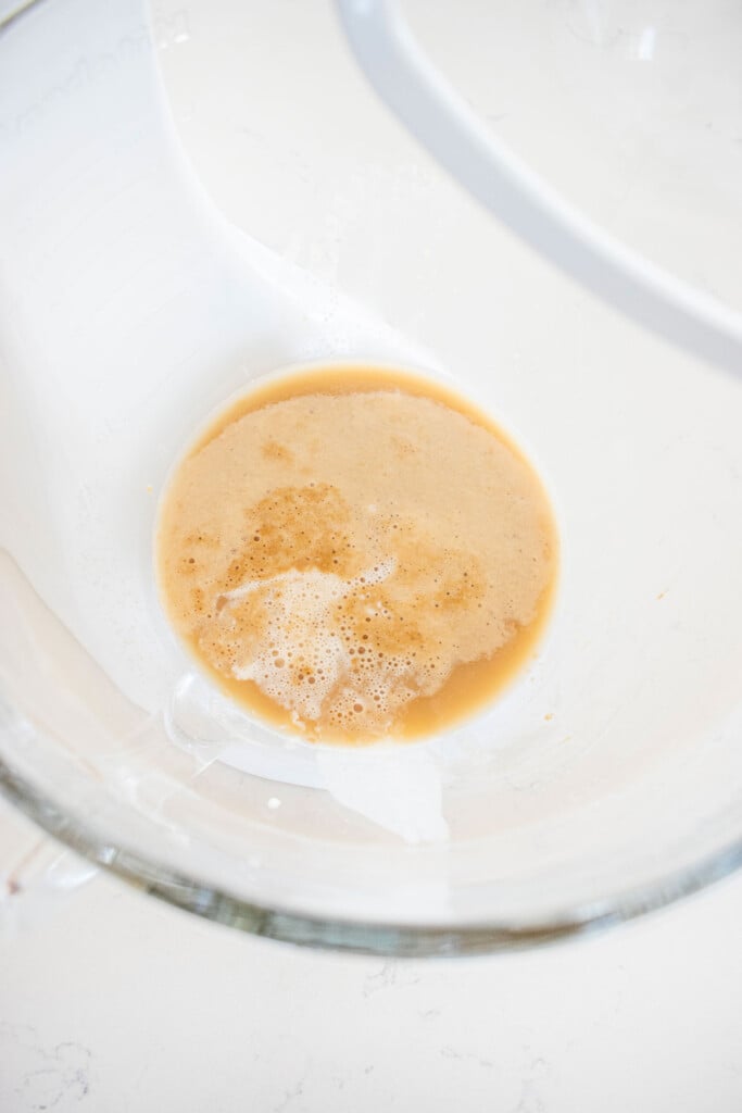 yeast and brown sugar in a glass mixing bowl on a white marble counter.