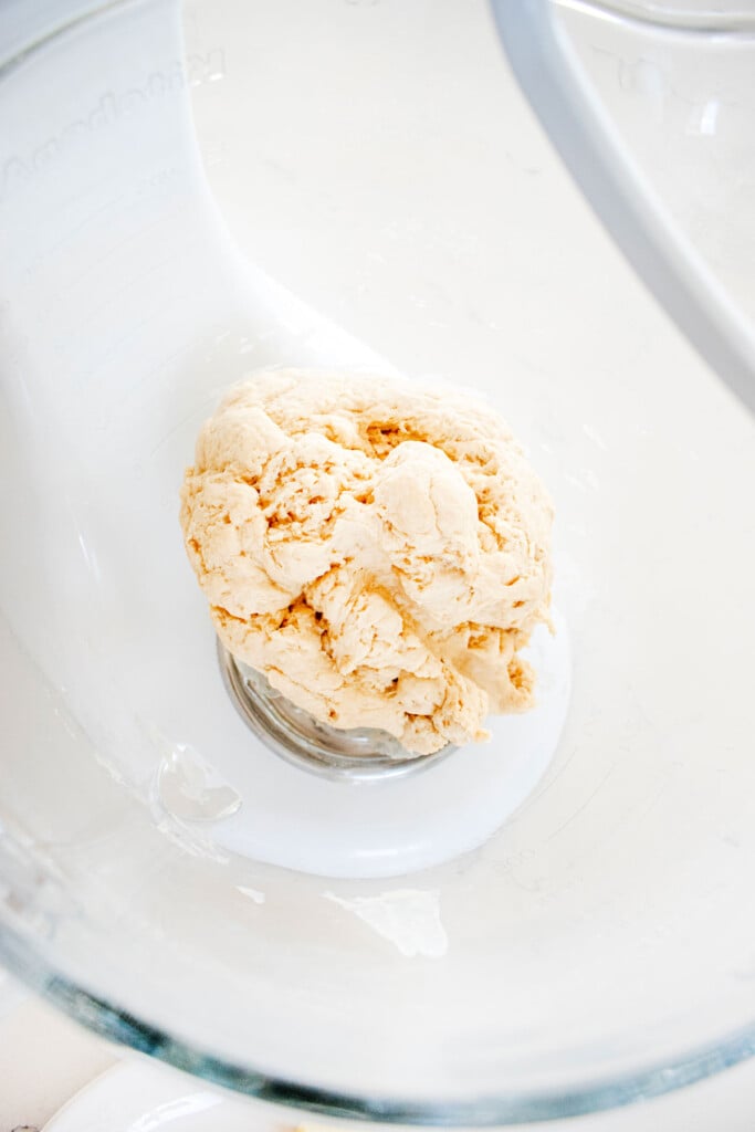 sourdough pretzel bun dough in a glass mixing bowl on a white marble counter.