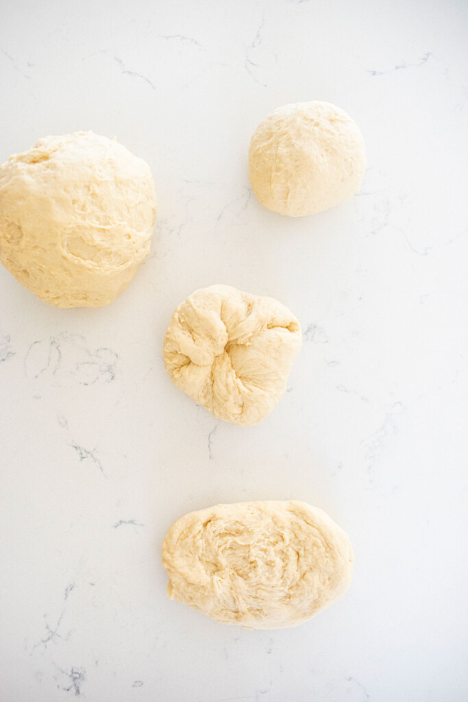 sourdough pretzel bun dough on a white marble counter being formed into balls.