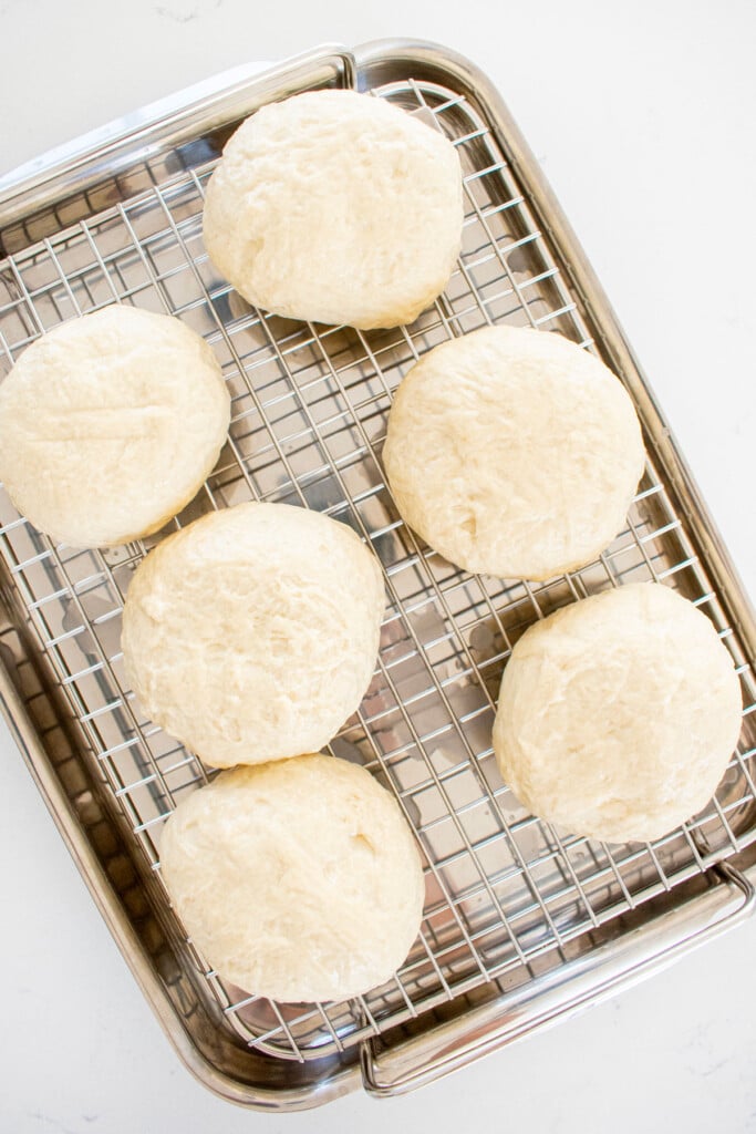 sourdough pretzel bun dough on a cooling rack on a white marble counter.