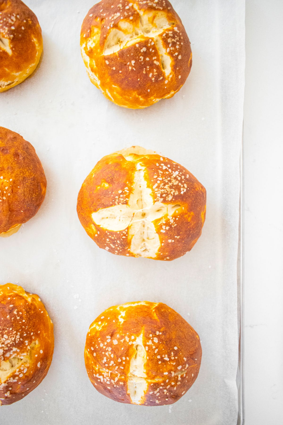sourdough pretzel buns on a baking sheet on a white marble counter.