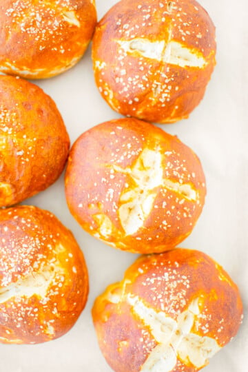 sourdough pretzel buns on a baking sheet on a white marble counter.