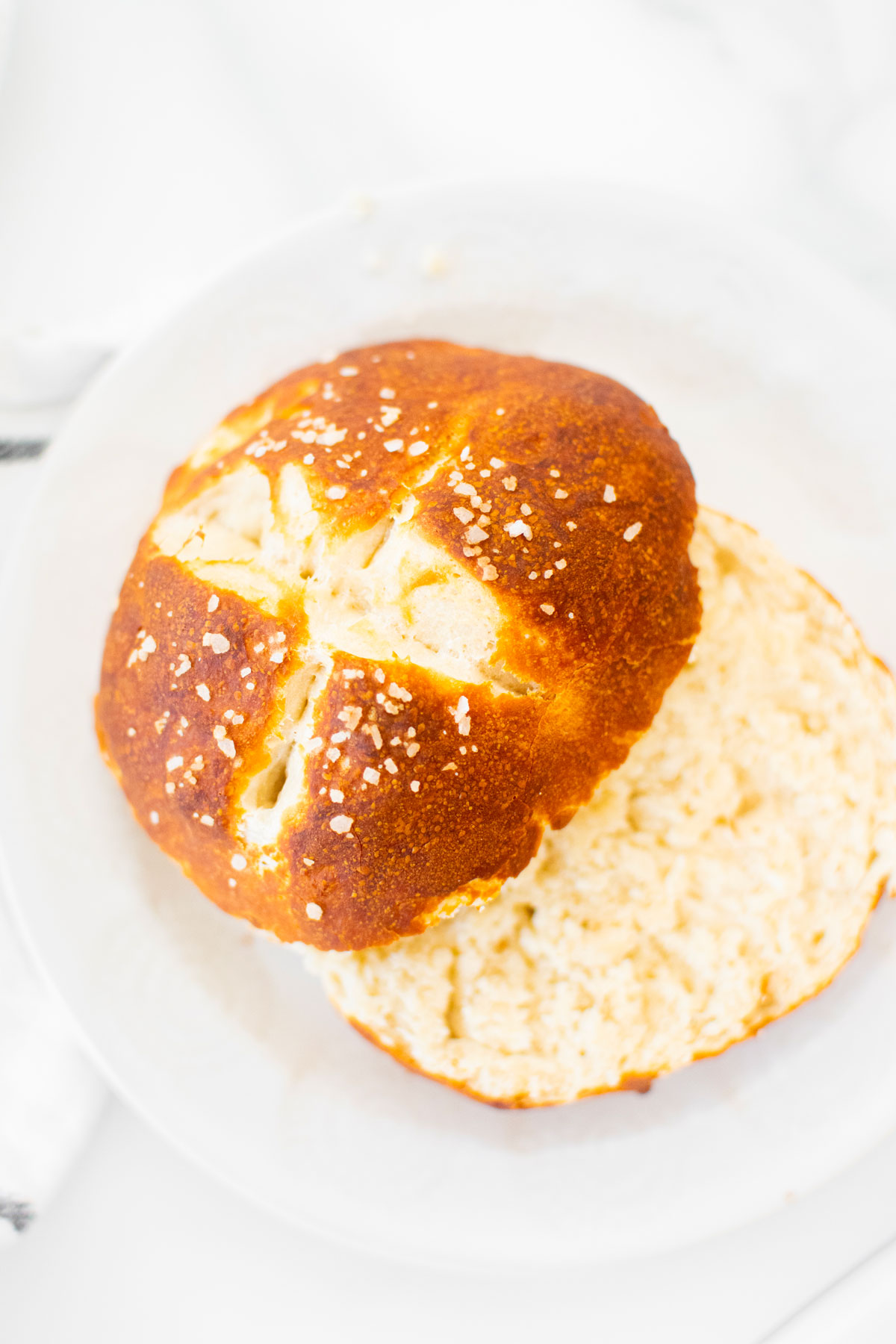 sourdough pretzel bun cut in half on a white plate.